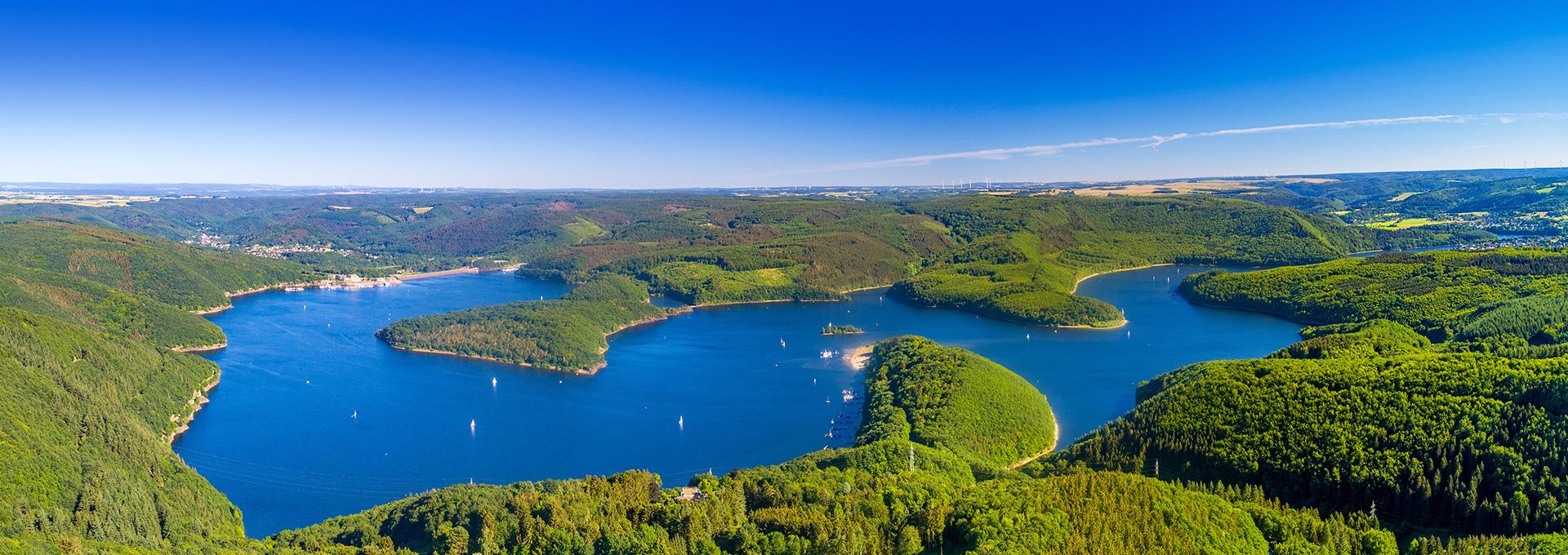 Panoramablick auf einen See mit bewaldeten Halbinseln und Hügeln in der Eifel